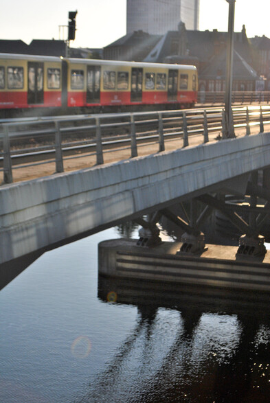 a train on a bridge over the river Spree with sunlight sparkling on the water below